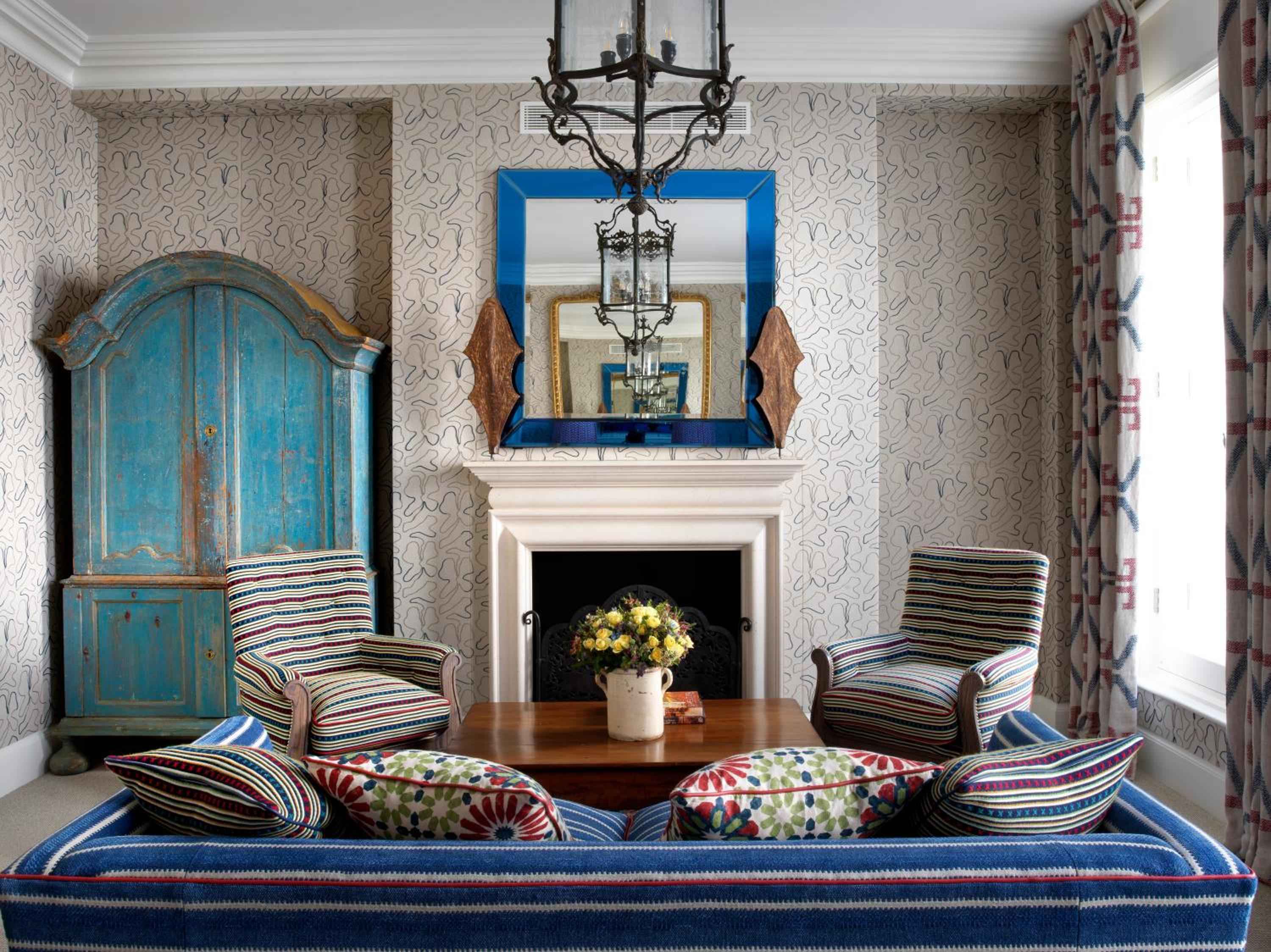 Striped armchairs frame a crackling fireplace while weathered blue armoire adds vintage charm to this perfectly curated sitting room sanctuary.