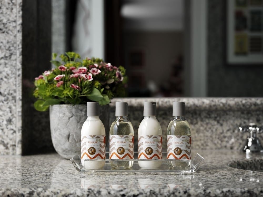 Luxurious toiletries from RIKRAK line granite surfaces beside delicate geraniums, where thoughtful details transform everyday moments into refined rituals of self-care.