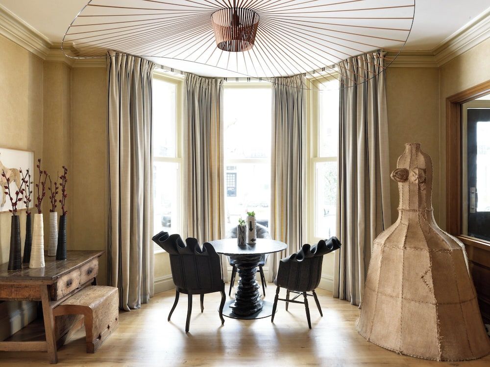 Sculptural black chairs gather beneath a striking wire pendant light in this intimate dining nook, where natural light filters through elegant striped curtains.
