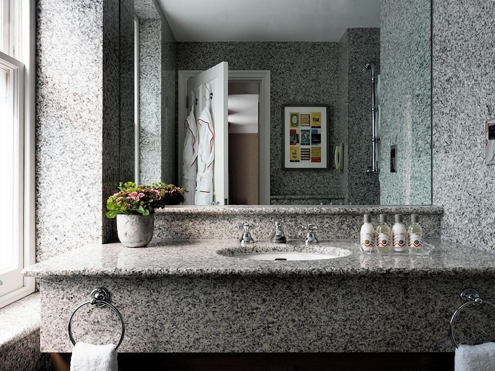 Speckled granite surfaces and chrome fixtures create a sophisticated powder room where natural light filters through sheer curtains, highlighting thoughtful touches like fresh blooms.