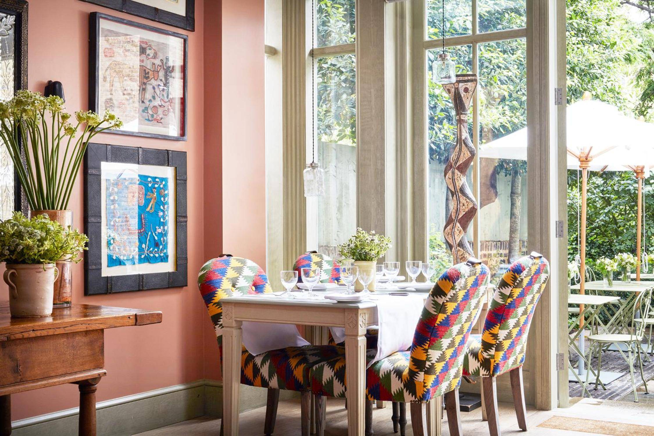 Vibrant kilim-upholstered chairs gather around an intimate table where afternoon light filters through Georgian windows, creating a bohemian-chic dining sanctuary.