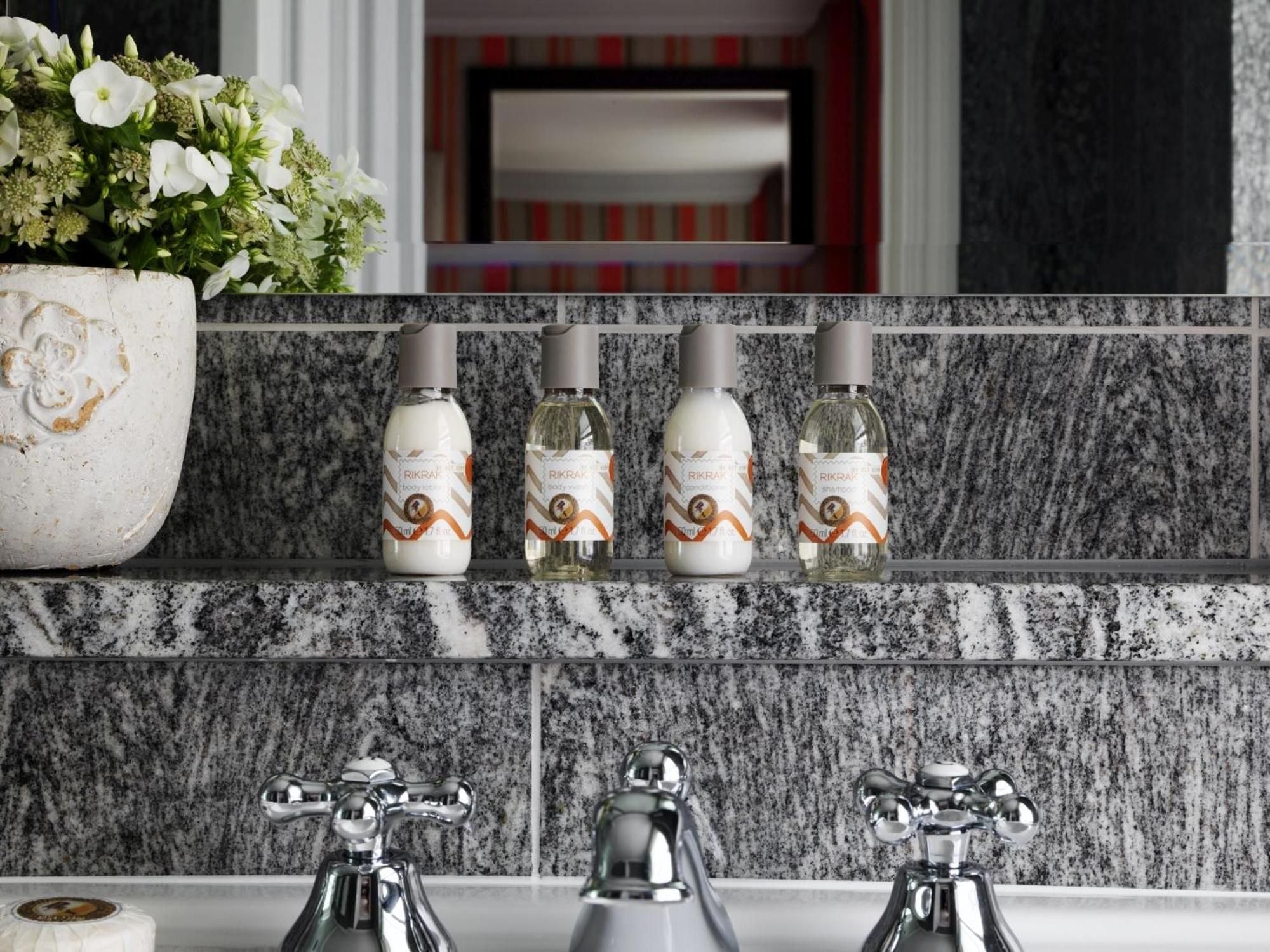 Vintage-style chrome taps gleam against speckled granite, while luxury amenities await on marble shelves—classic British elegance meets modern comfort in every thoughtful detail.
