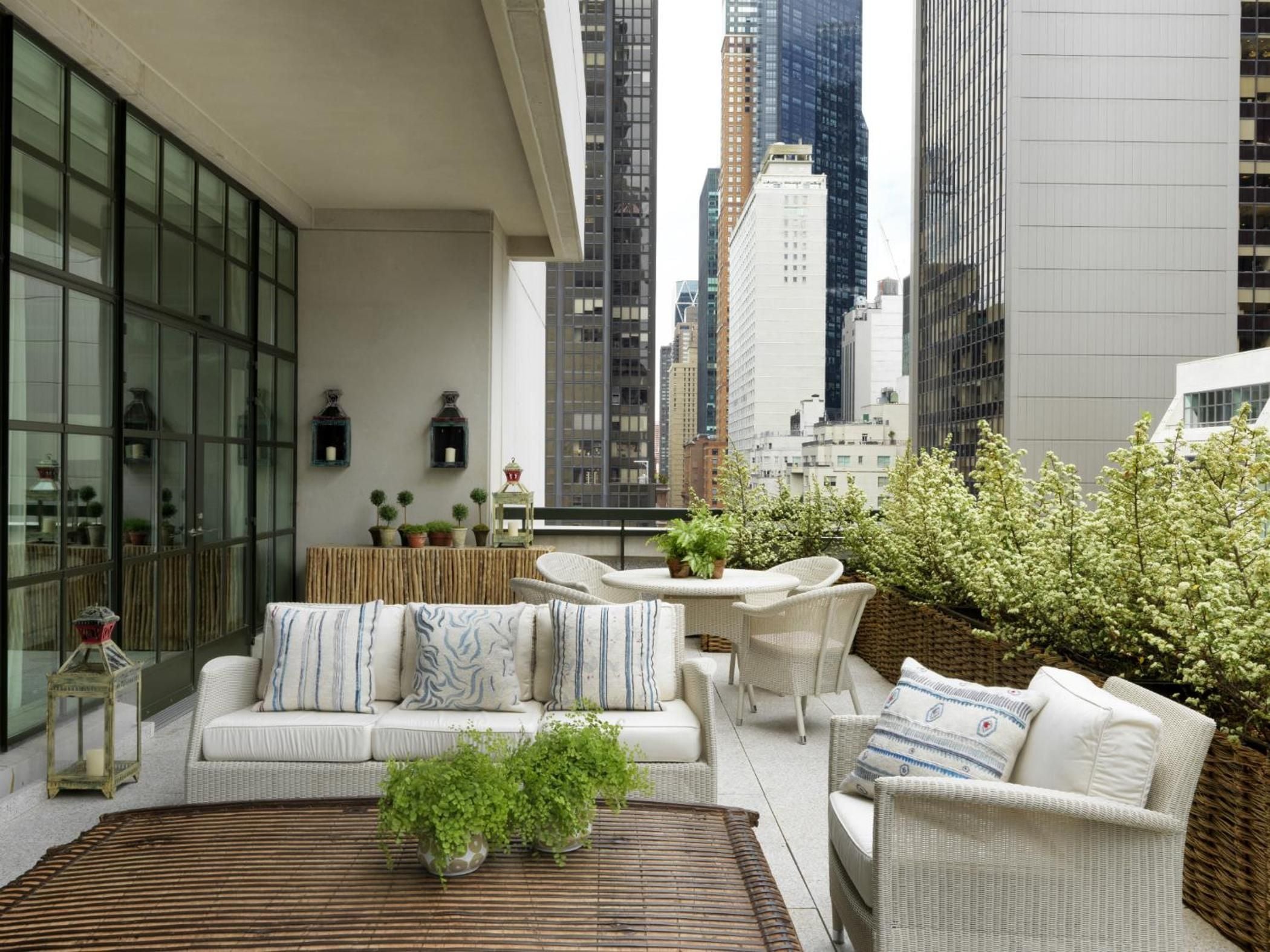 Wicker seating and blue-striped pillows create an intimate outdoor living room high above Midtown's soaring towers, where city energy meets terrace tranquility.