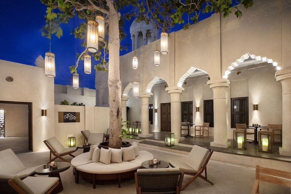 Hanging lanterns cast a golden glow over the serene courtyard where ancient sycamore trees rise through carved arches, creating an oasis of Moorish elegance.