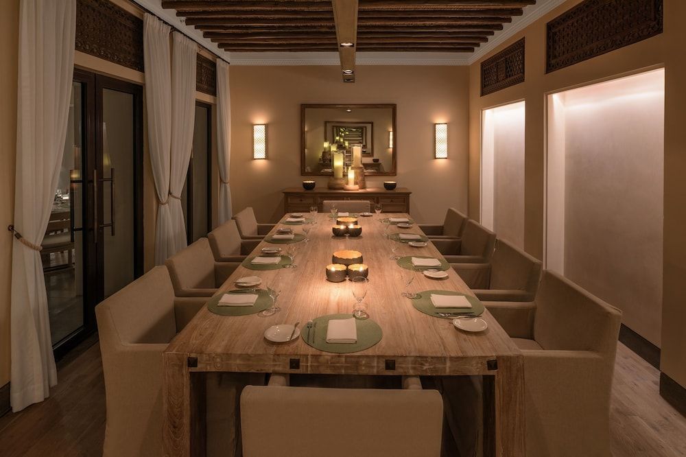 Warm candlelight dances across the polished wood table in this intimate private dining room, where exposed ceiling beams and soft curtains create an atmosphere of understated luxury.