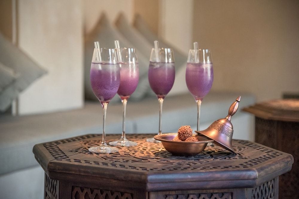 Purple-hued cocktails catch golden light on an intricately carved wooden table, while copper bar tools hint at the artisanal craft behind each handcrafted libation.
