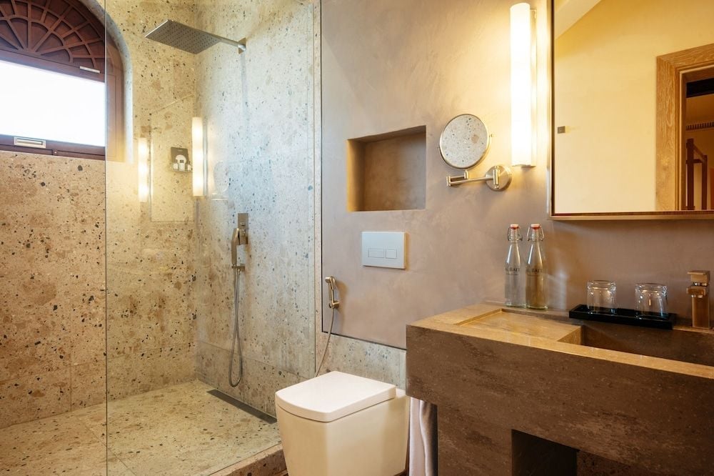 Natural stone walls and warm lighting create a spa-like sanctuary where rain showers and handcrafted amenities transform daily rituals into moments of pure indulgence.