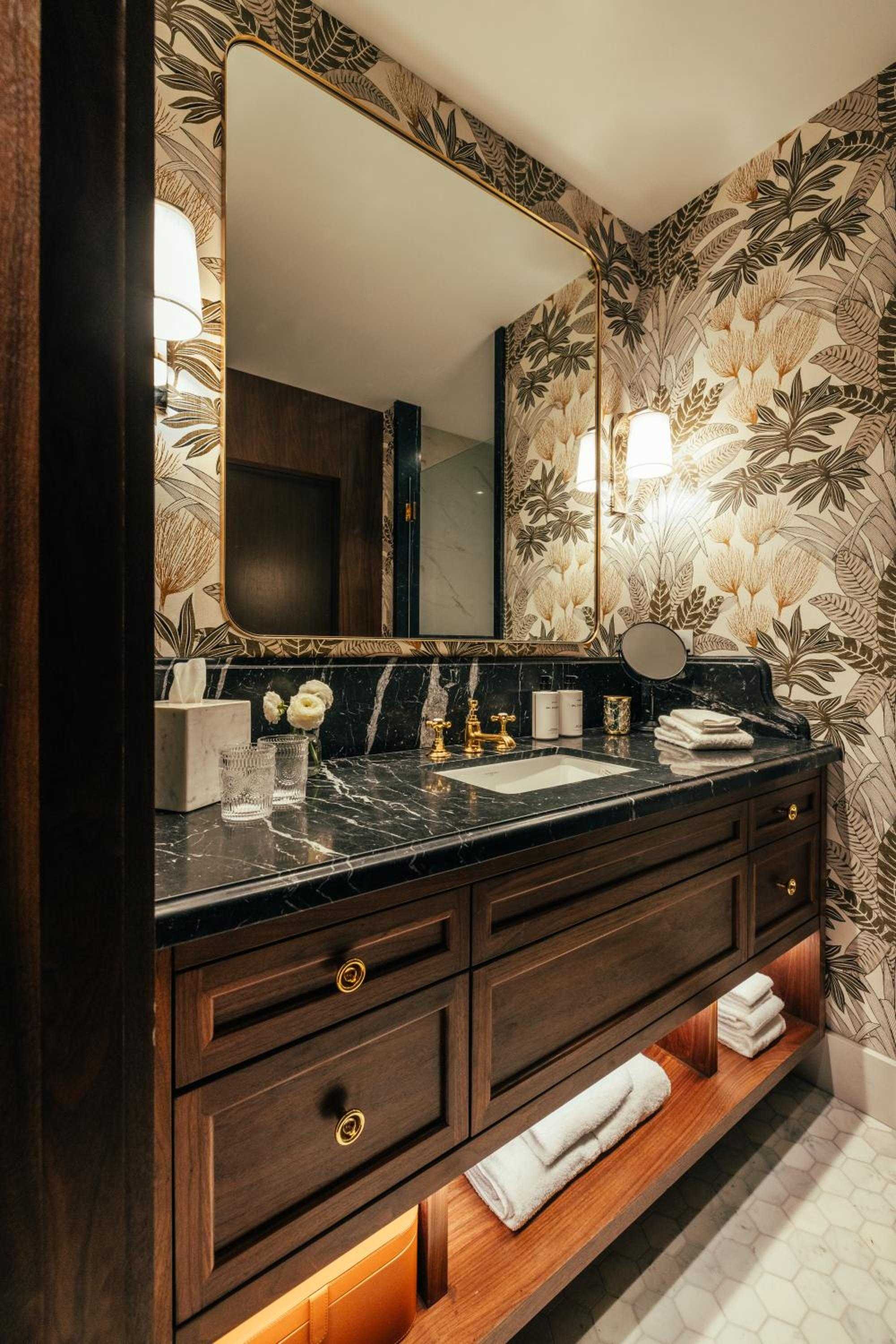 Botanical wallpaper blooms against rich walnut cabinetry while black marble countertops and brass fixtures create an opulent powder room that feels like a jewel box.