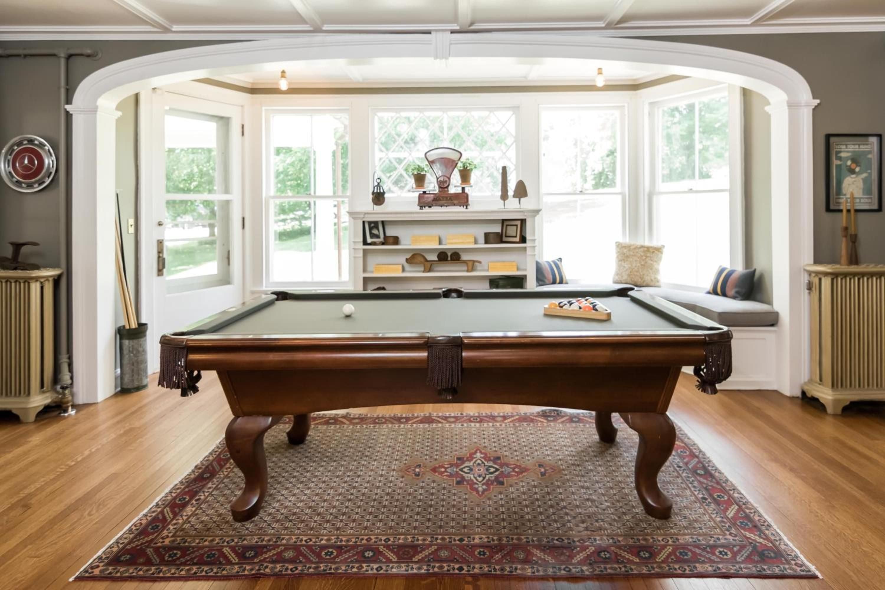 Polished hardwood floors gleam beneath an elegant billiards table, where afternoon light streams through bay windows onto built-in seating and vintage furnishings.