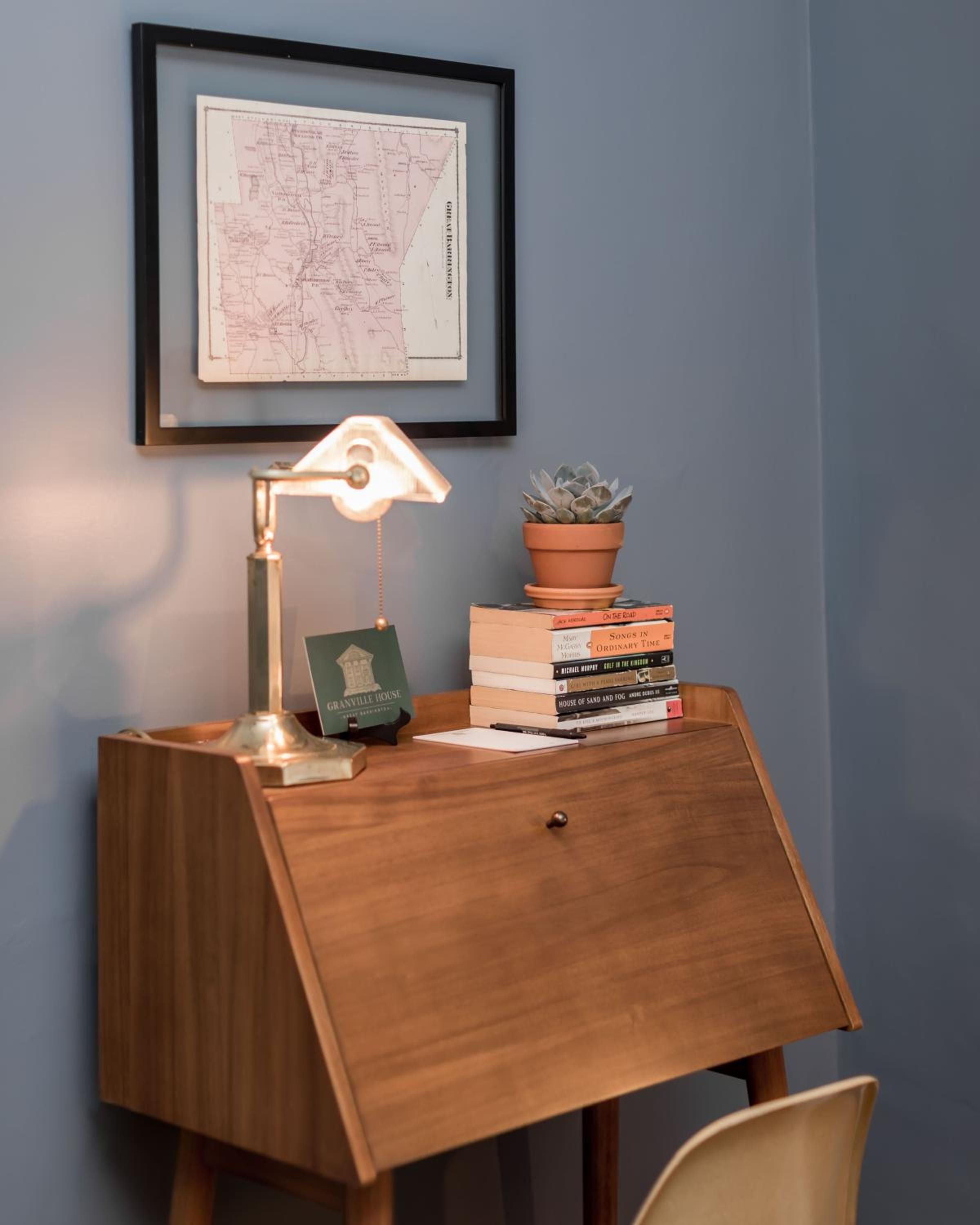 Mid-century walnut desk bathed in golden lamplight creates an intimate writing nook, complete with curated books and a thriving succulent companion.