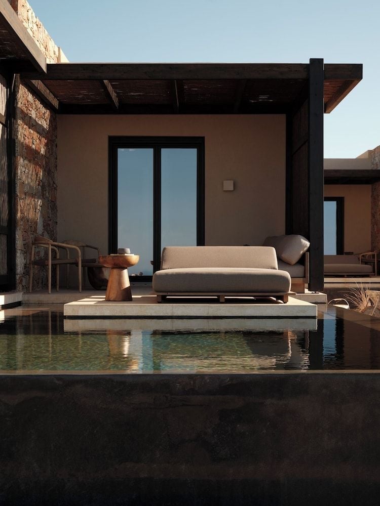 Minimalist elegance meets Mediterranean warmth as neutral furnishings float above crystalline waters, creating an oasis where stone, wood, and sky converge in perfect harmony.