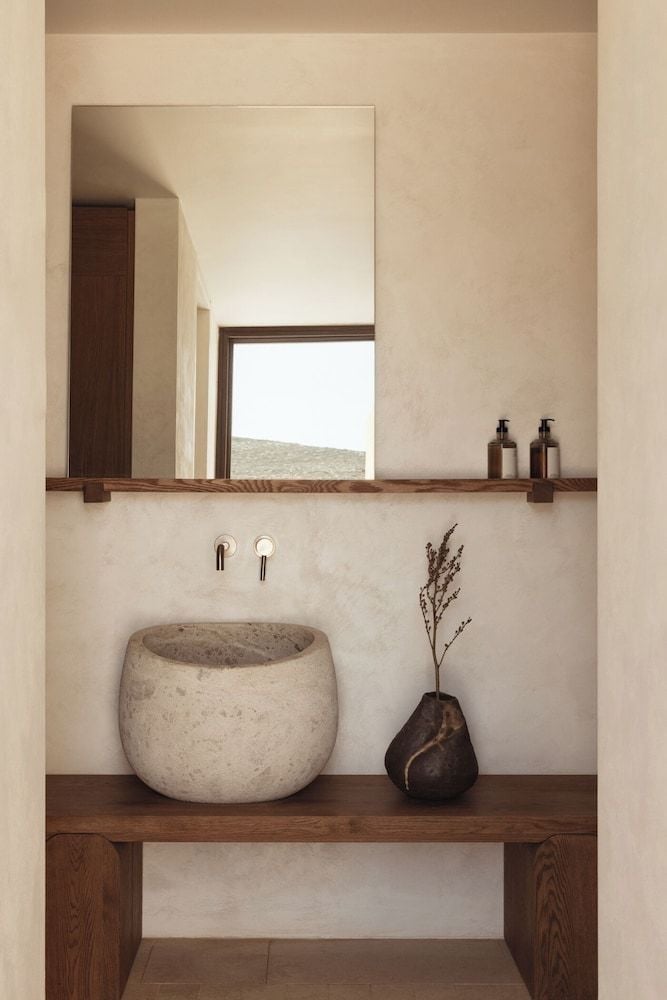 Natural stone meets warm wood in this serene powder room, where handcrafted ceramics and golden light create an intimate sanctuary of earthen luxury.