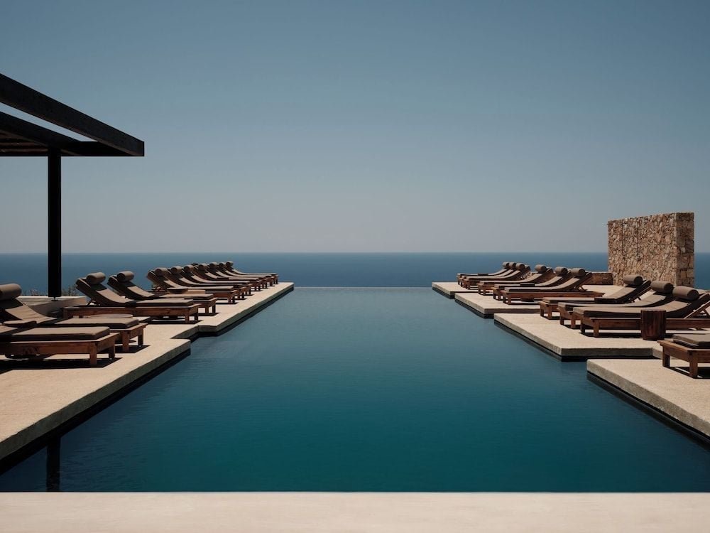 Infinity waters mirror the Aegean horizon while teak loungers frame this clifftop sanctuary, where minimalist architecture meets the endless Mediterranean blue.