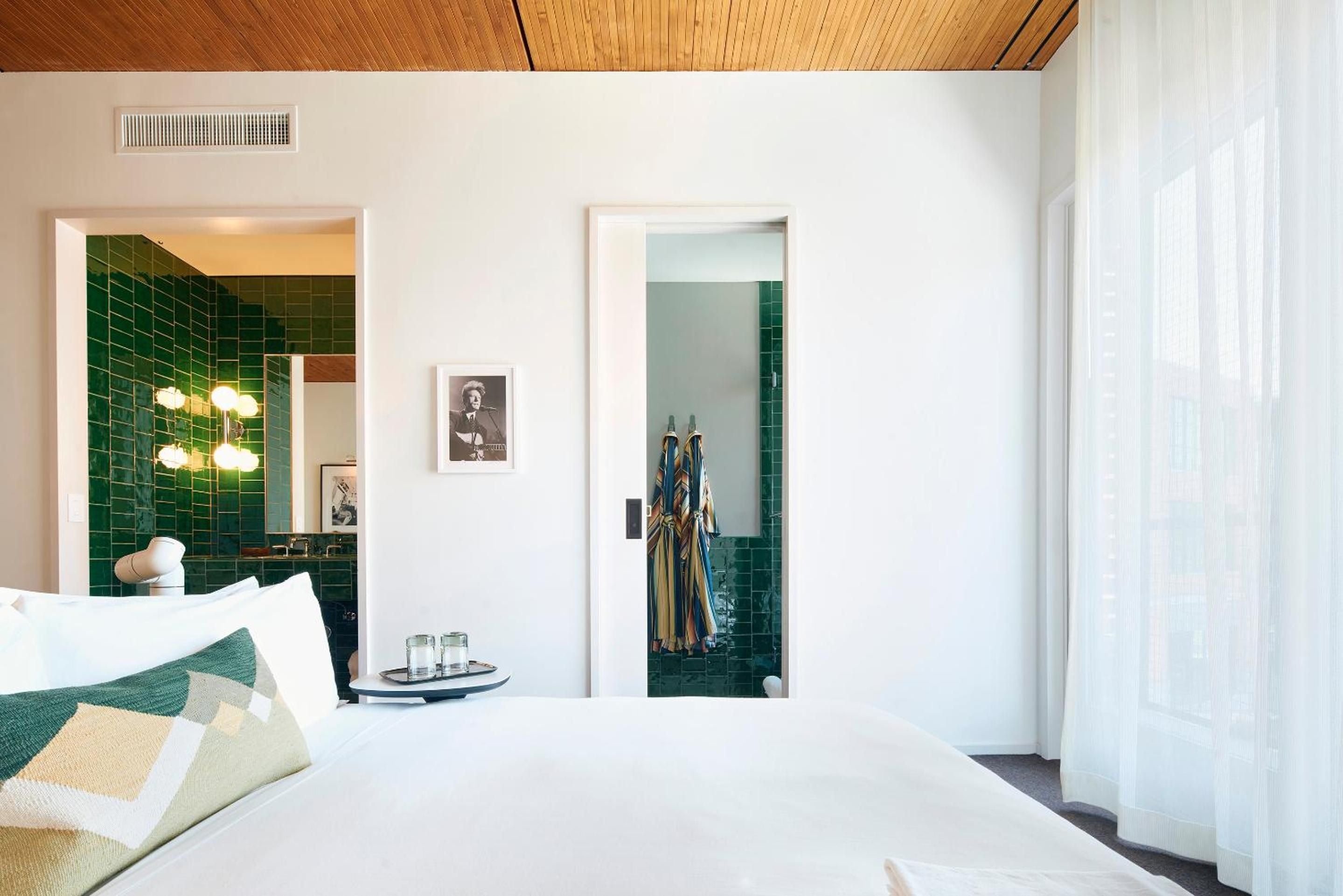 Emerald subway tiles create a jewel-box bathroom beyond crisp white linens, while warm wood ceilings add organic texture to this thoughtfully curated guest room.