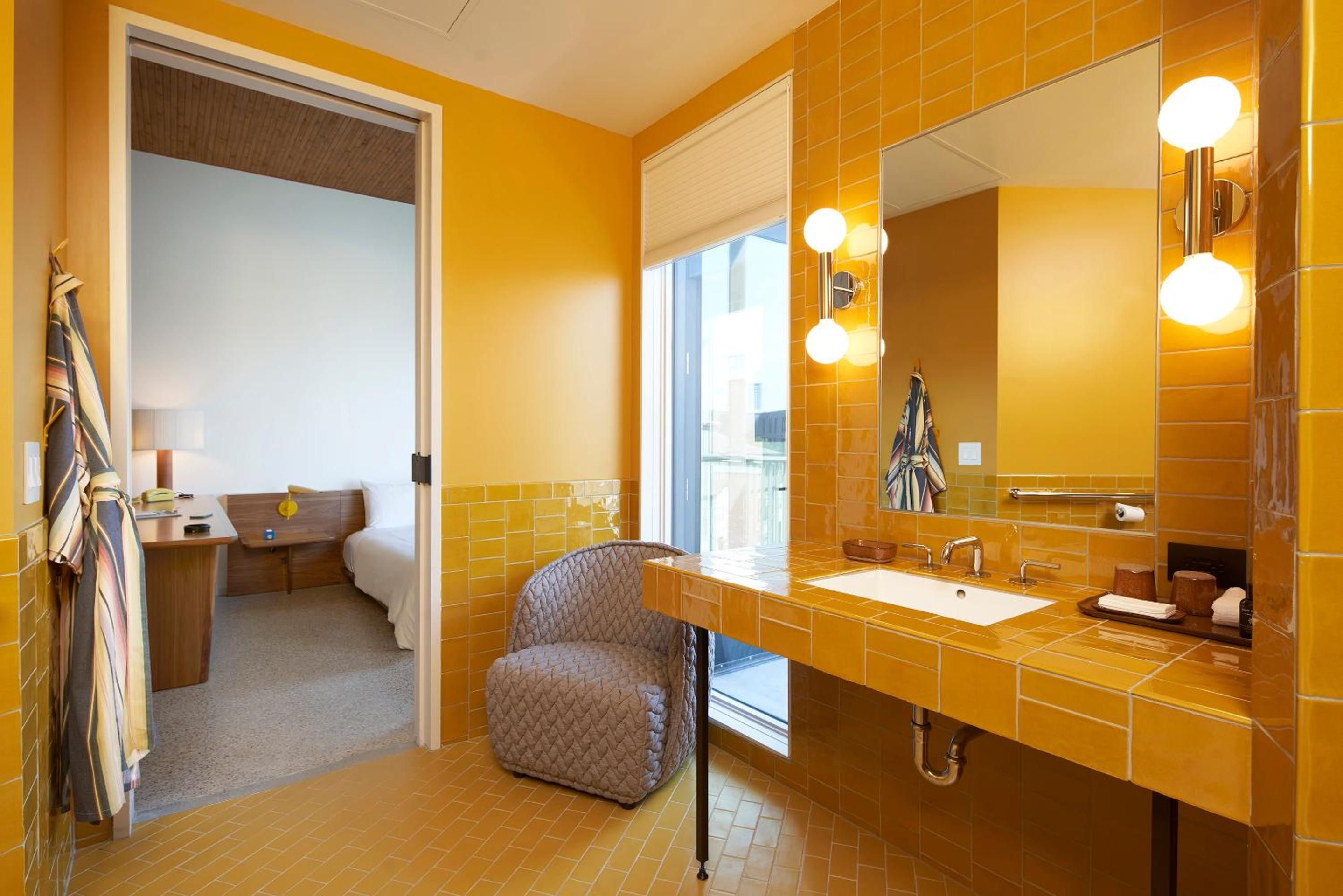 Vibrant golden tiles catch morning light in this mid-century inspired bathroom, where a quilted vanity chair and floating sink create an unexpectedly glamorous getting-ready ritual.