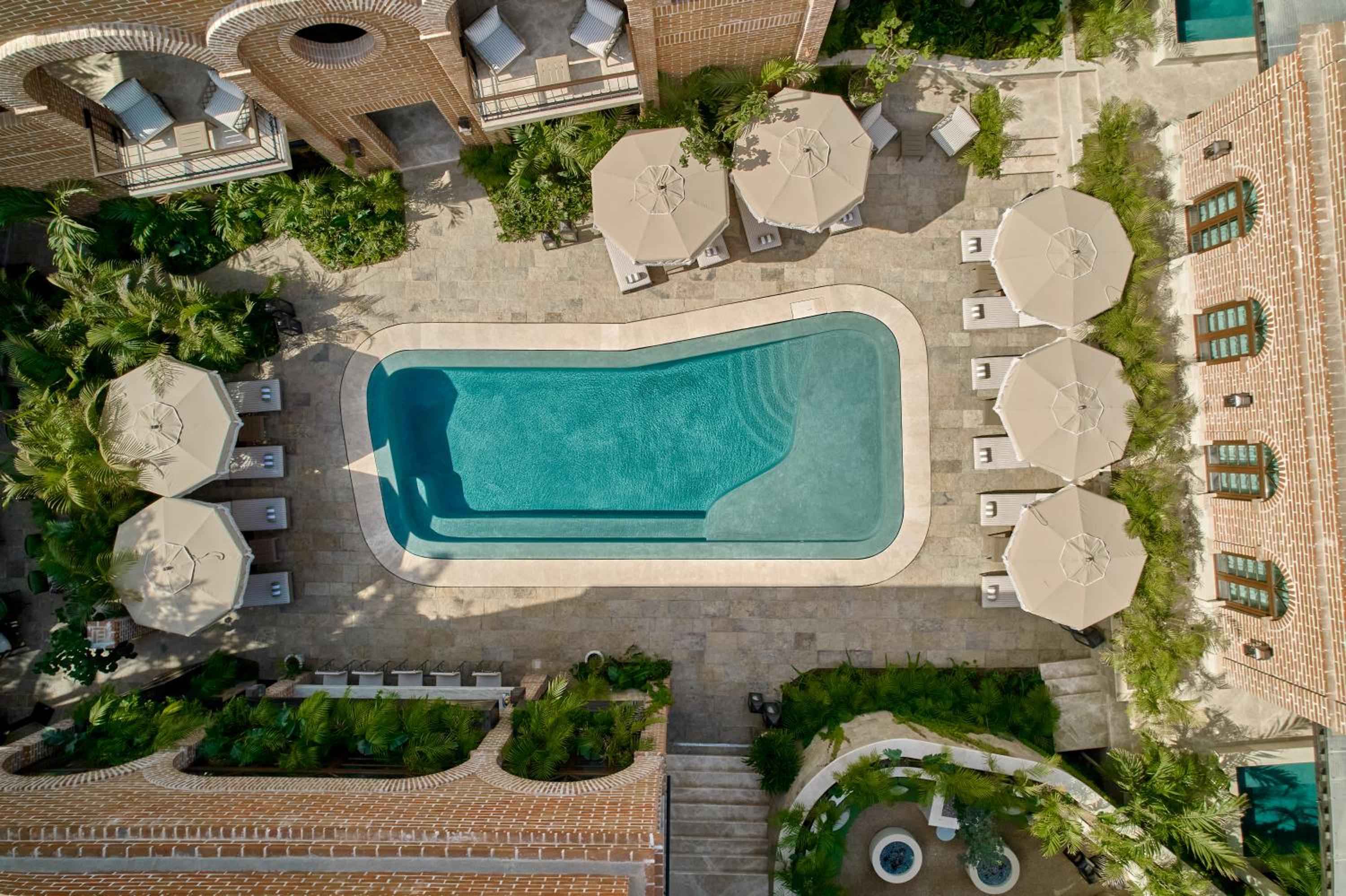 Palm trees cast dappled shadows across terracotta tiles as beige umbrellas frame the crystalline pool, creating an intimate Mediterranean-inspired courtyard sanctuary.