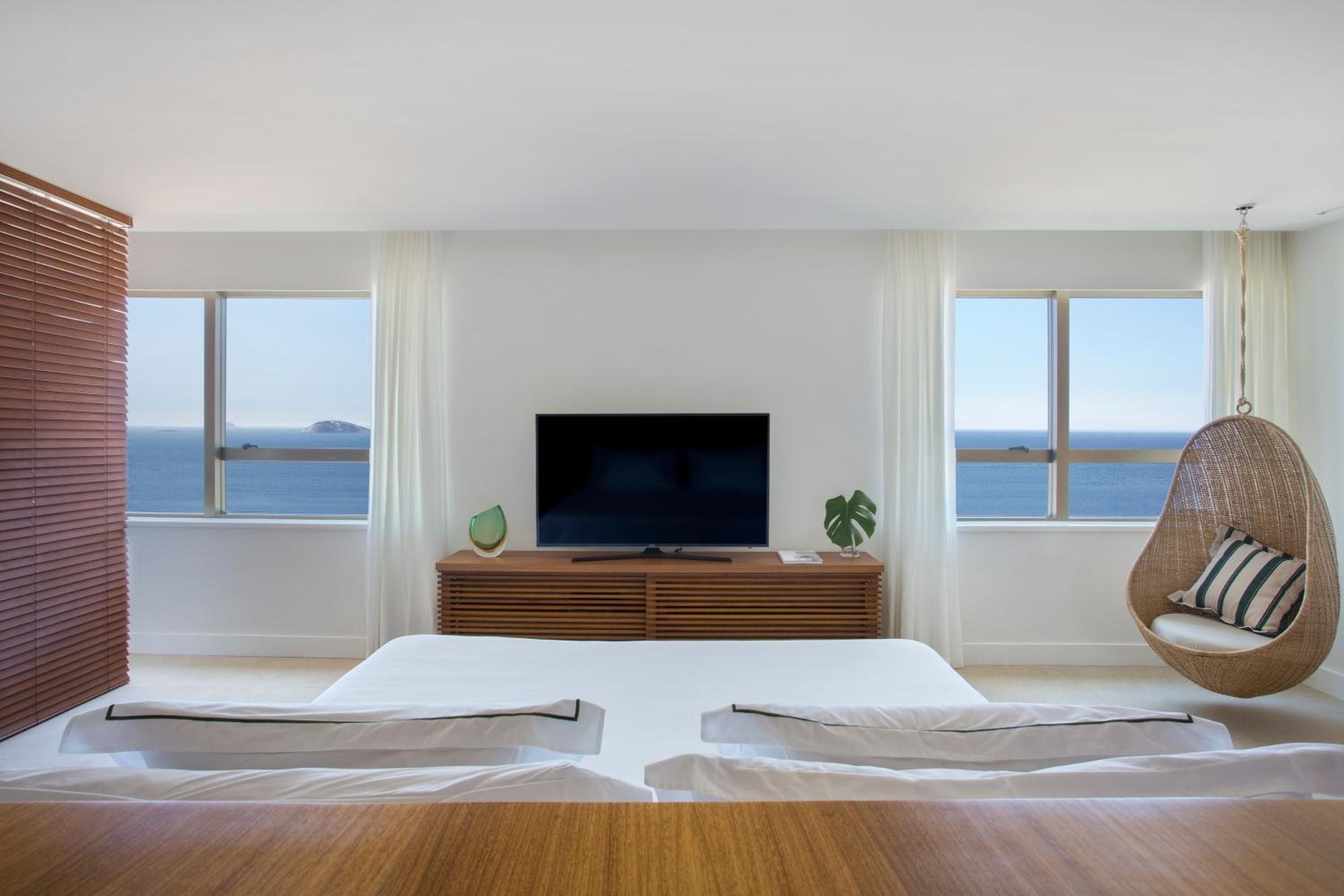 Crisp white linens frame panoramic ocean views while a woven hanging chair and warm wood media console create an effortlessly sophisticated coastal retreat.