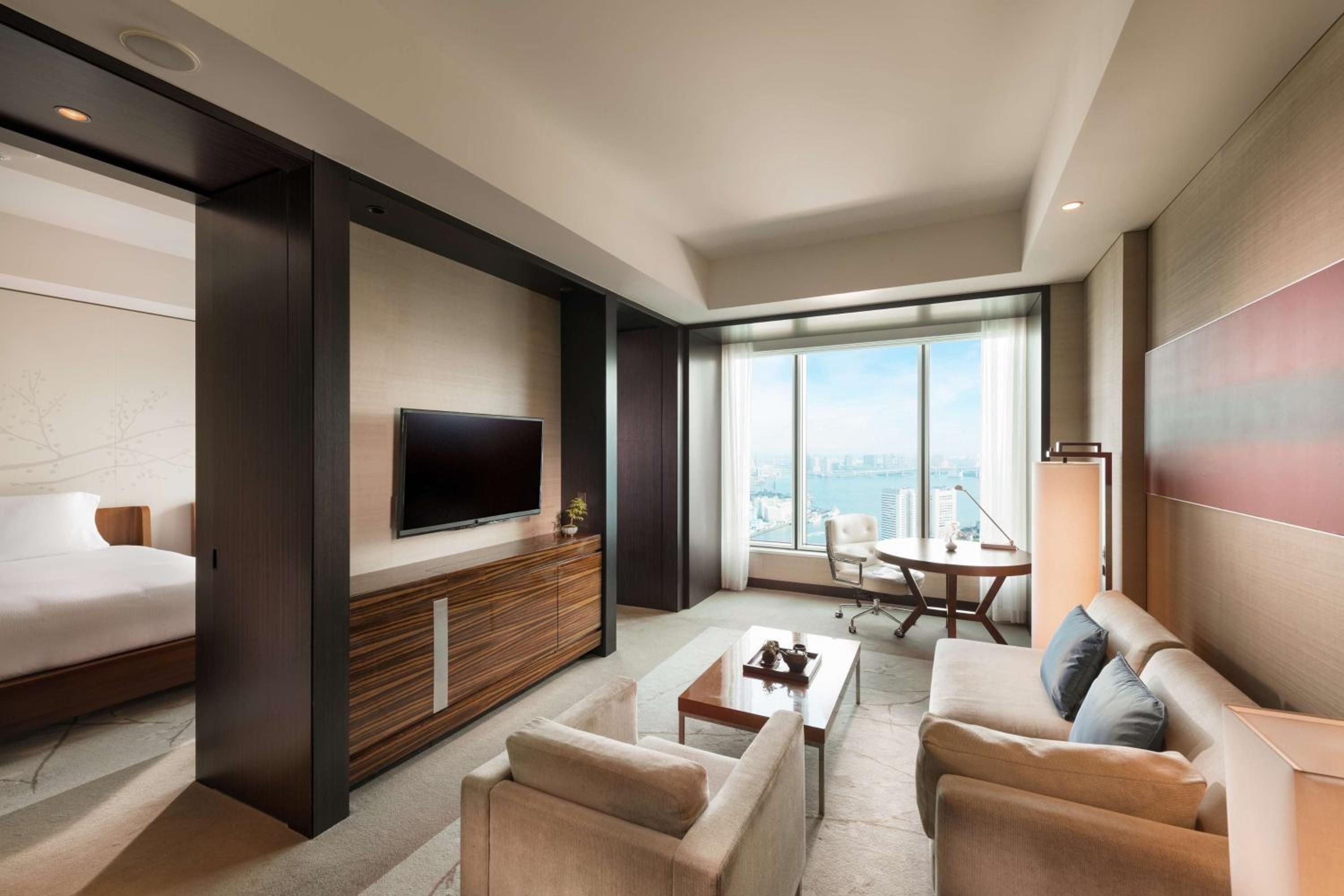 Floor-to-ceiling windows frame Tokyo's sprawling cityscape from this sophisticated suite, where warm wood tones and plush seating create an intimate urban sanctuary.