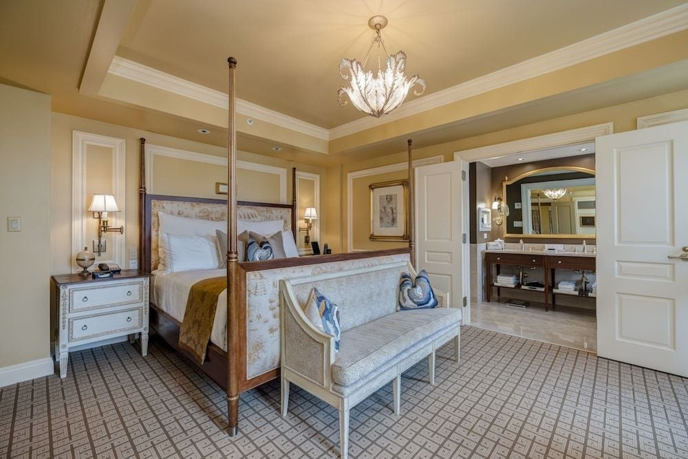 Coffered ceilings and crystal chandeliers create an air of refined elegance in this spacious suite, where a four-poster bed anchors the luxurious bedroom space.