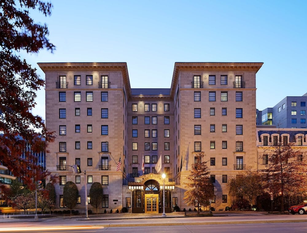 Classic limestone towers rise majestically against the evening sky, their warm-lit windows creating an inviting beacon amid Washington's sophisticated streetscape.