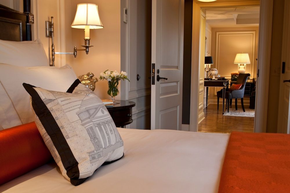 Crisp linens meet warm lamplight in this elegantly appointed suite, where architectural blueprint pillows add whimsical character to classic sophistication.