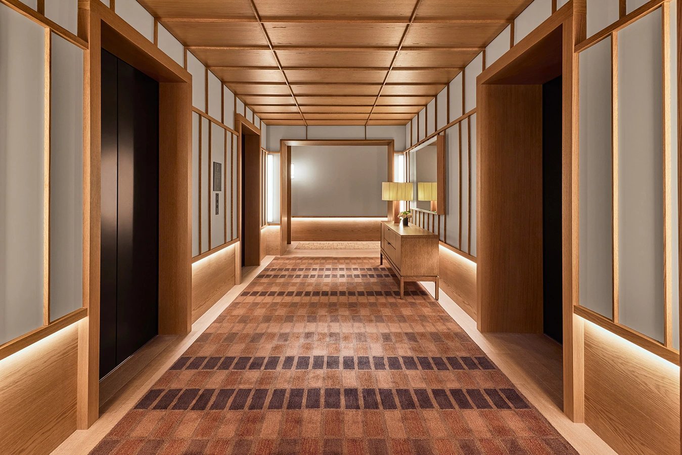 Warm wood paneling and geometric carpeting create an inviting corridor where soft ambient lighting guides guests through thoughtfully designed transitional spaces.