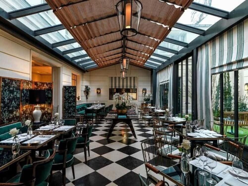 Checkered marble floors and emerald velvet banquettes create Parisian bistro glamour beneath the glass-roofed conservatory, where lantern light dances across botanical wallpaper.