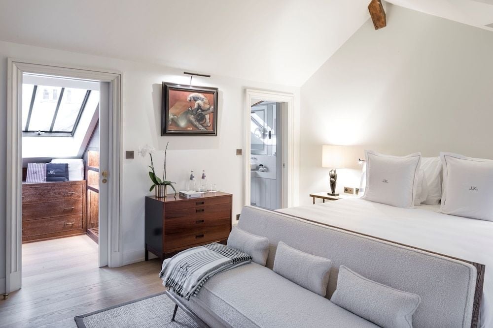 Exposed wooden beams frame this elegant attic suite, where mid-century furnishings and soft linens create an intimate Parisian retreat bathed in natural light.