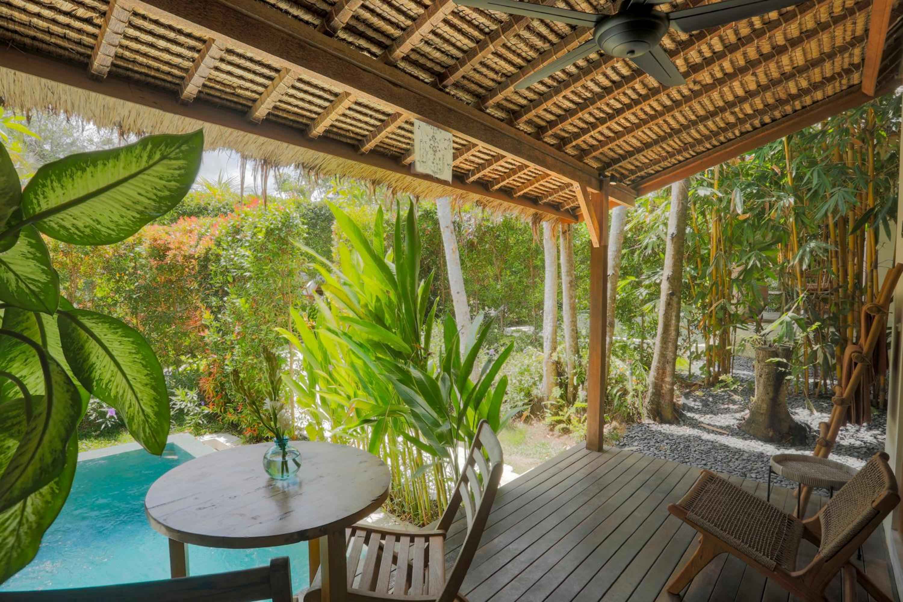 Bamboo rafters and thatched textures frame this intimate poolside pavilion, where tropical greenery spills into view and carved wooden furnishings invite languid afternoon moments.