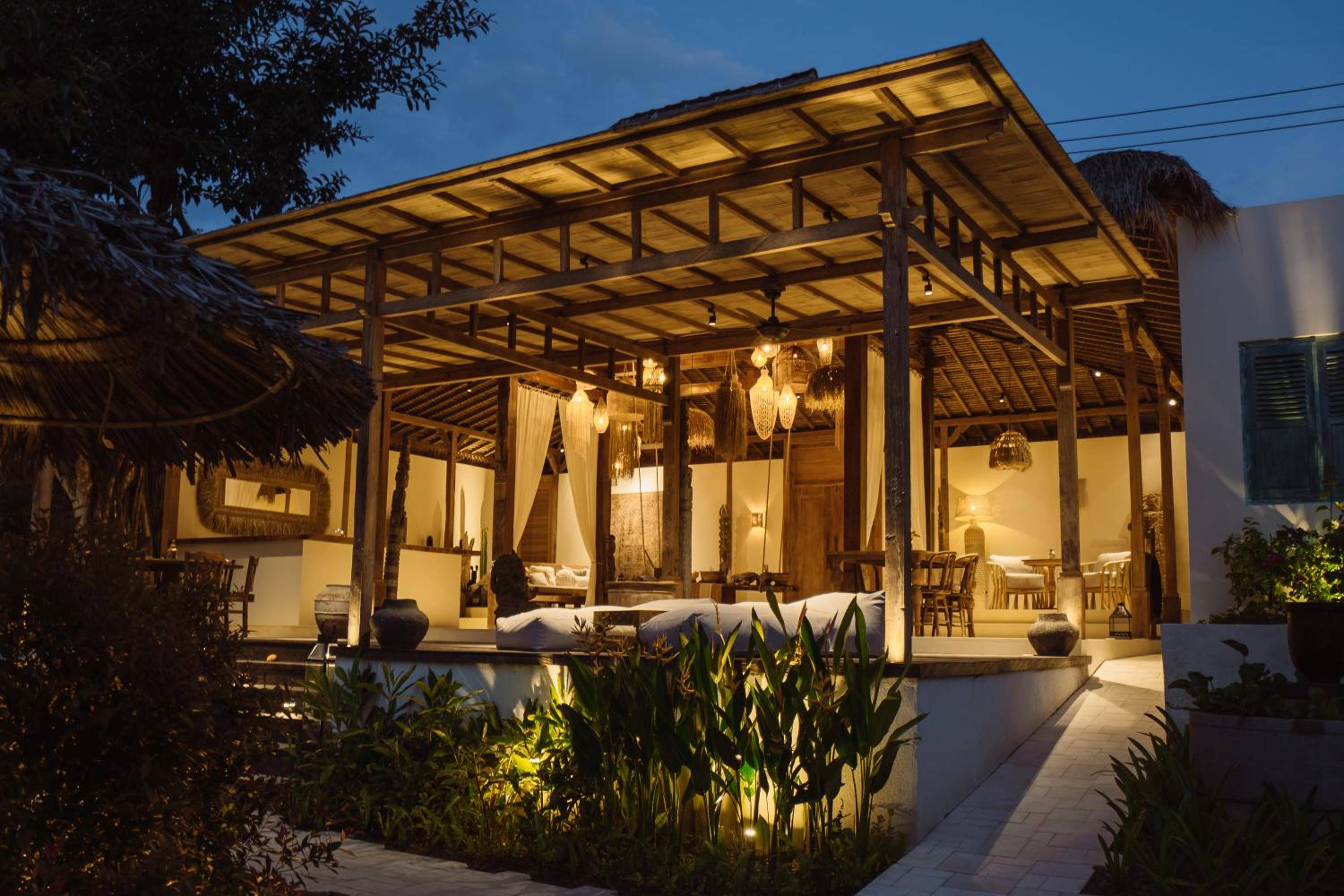 Bamboo beams frame this elevated pavilion suite where warm lighting spills across teak floors and tropical gardens whisper below in the evening breeze.