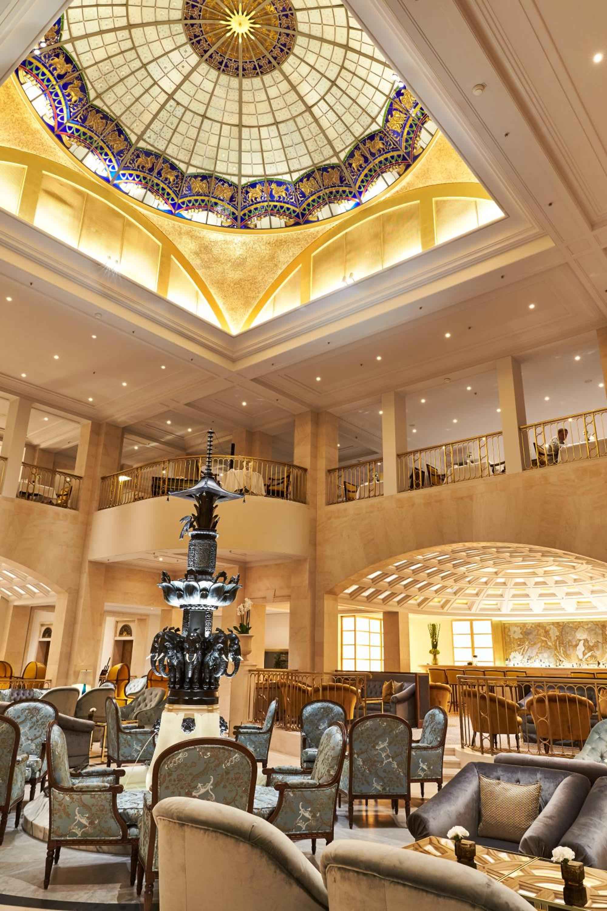 Sunlight streams through the magnificent glass dome, illuminating ornate Byzantine-inspired details and plush seating in this palatial lobby space where Berlin's grandest hospitality traditions unfold.