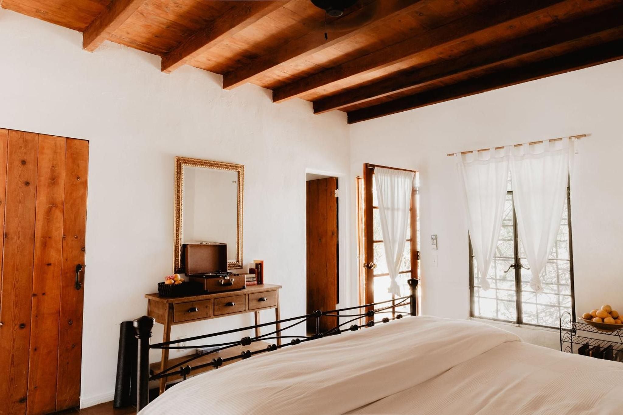 Exposed wooden beams crown this intimate bedroom where rustic charm meets refined comfort, white linens contrasting beautifully with warm timber and wrought iron details.
