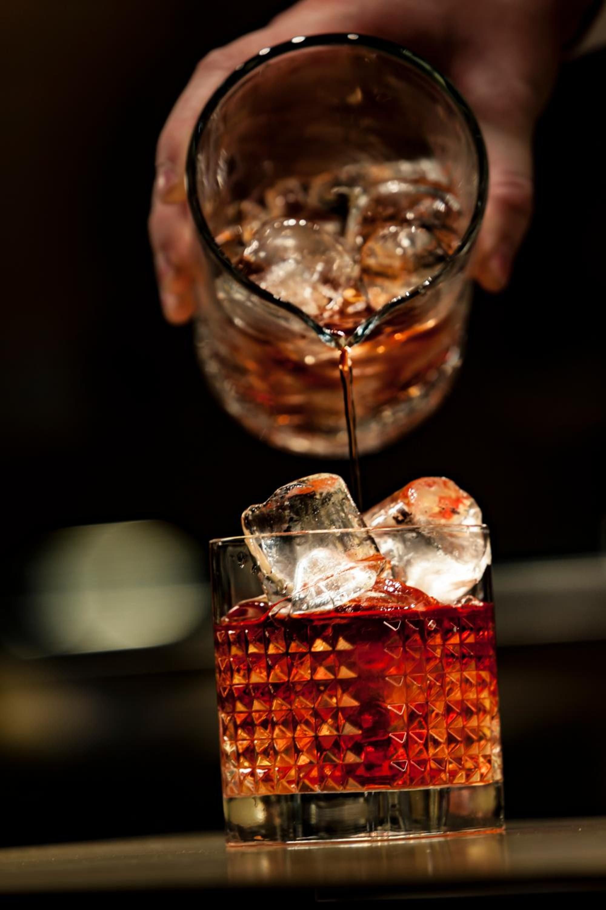 Crystal glasses catch warm amber light as premium spirits flow over hand-cut ice, creating an intimate evening ritual in the hotel's sophisticated bar setting.