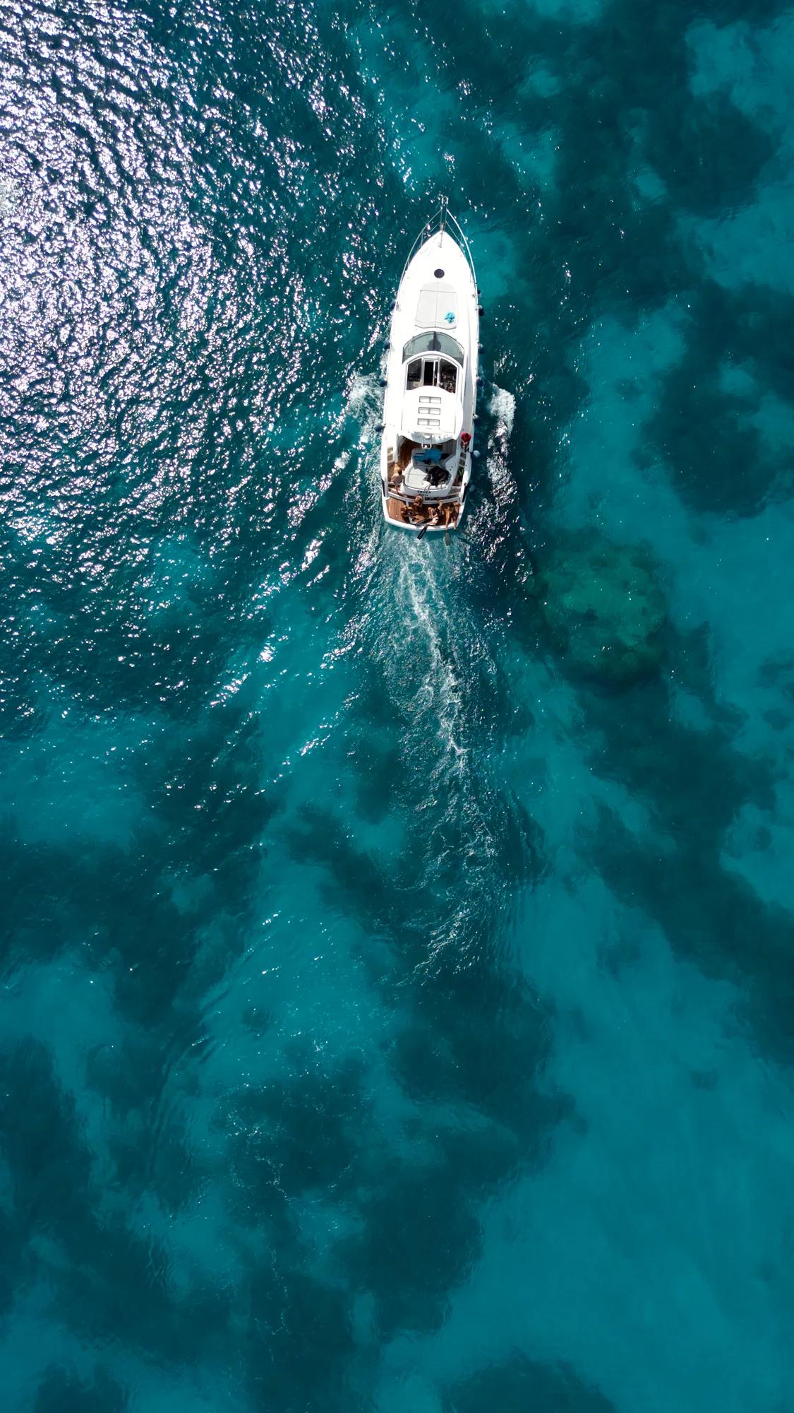Crystal-clear turquoise waters reveal their depths as a sleek white yacht cuts through the Mediterranean, leaving gentle ripples in its pristine wake.