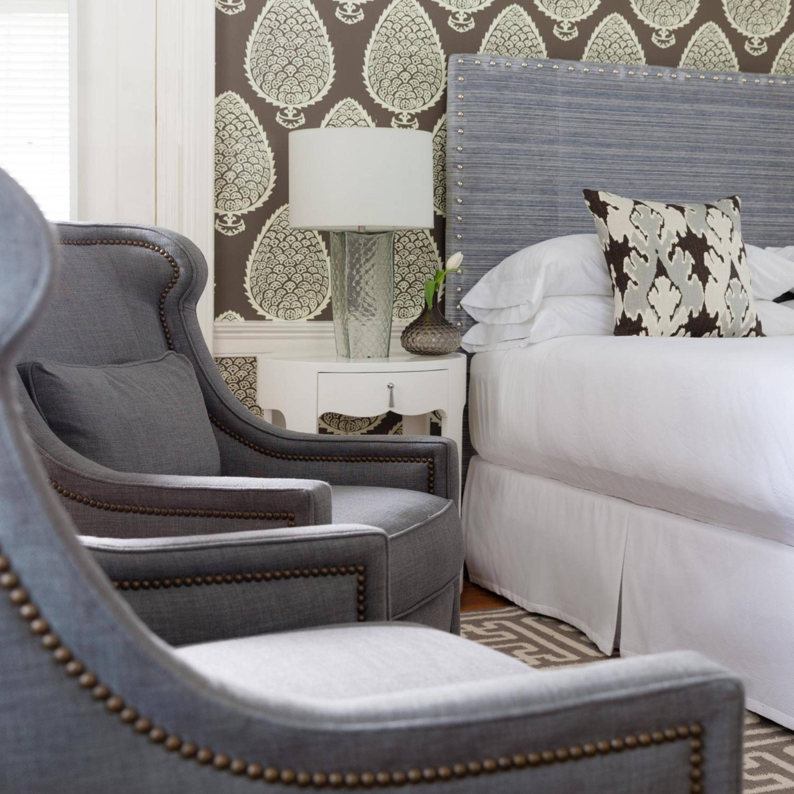 Nautical sophistication meets New England charm in guest rooms where weathered wood headboards and geometric wallpaper create intimate coastal elegance.