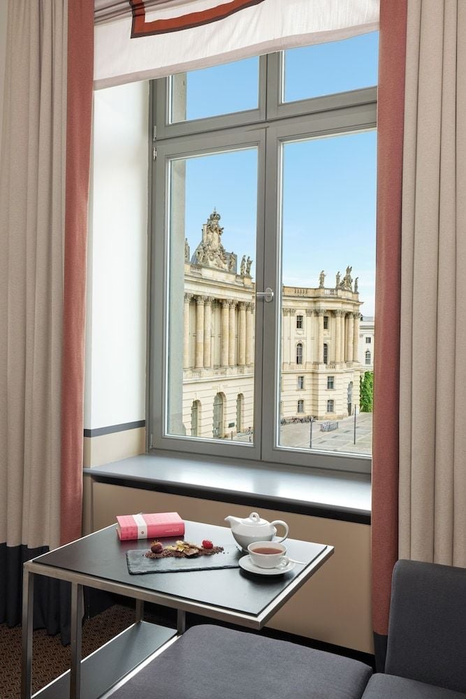 Morning light filters through floor-to-ceiling windows revealing Berlin's neoclassical Staatsoper, while afternoon tea awaits on polished marble surfaces.