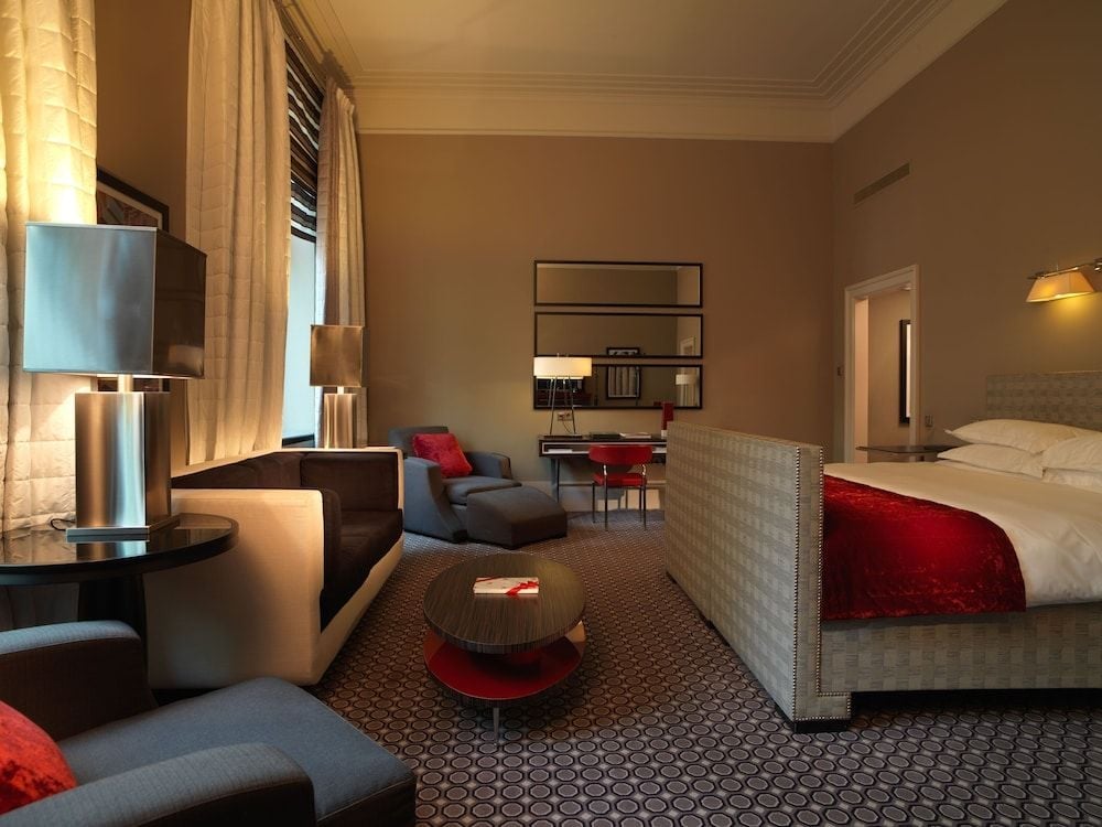 Warm amber lighting and geometric carpeting create intimate luxury in this spacious suite, where modern furnishings meet timeless elegance beneath soaring ceilings.