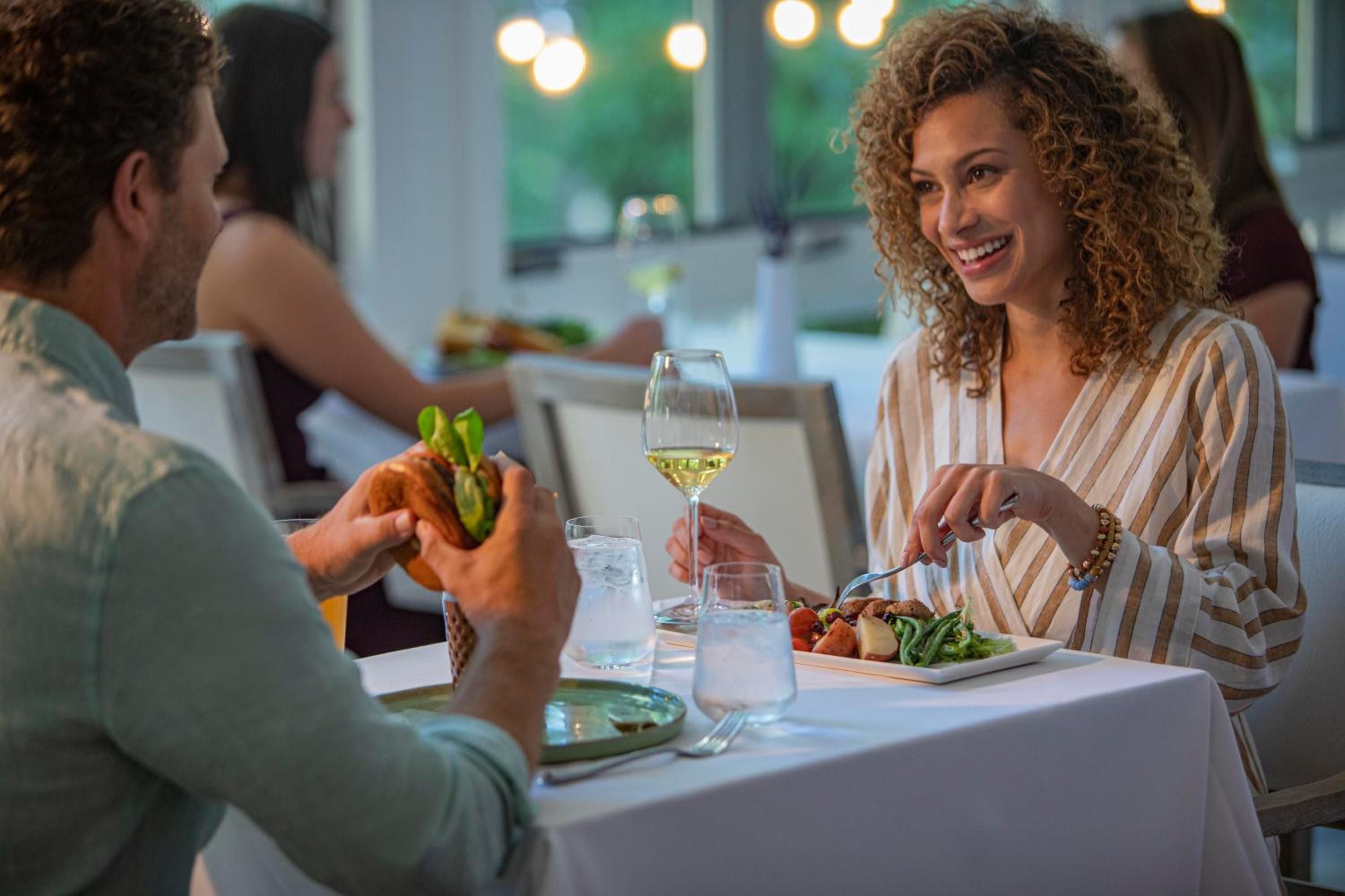 Intimate dining unfolds in warm lamplight as guests share fresh seasonal cuisine and crisp white wine, creating L'Auberge's signature blend of rustic elegance and genuine hospitality.