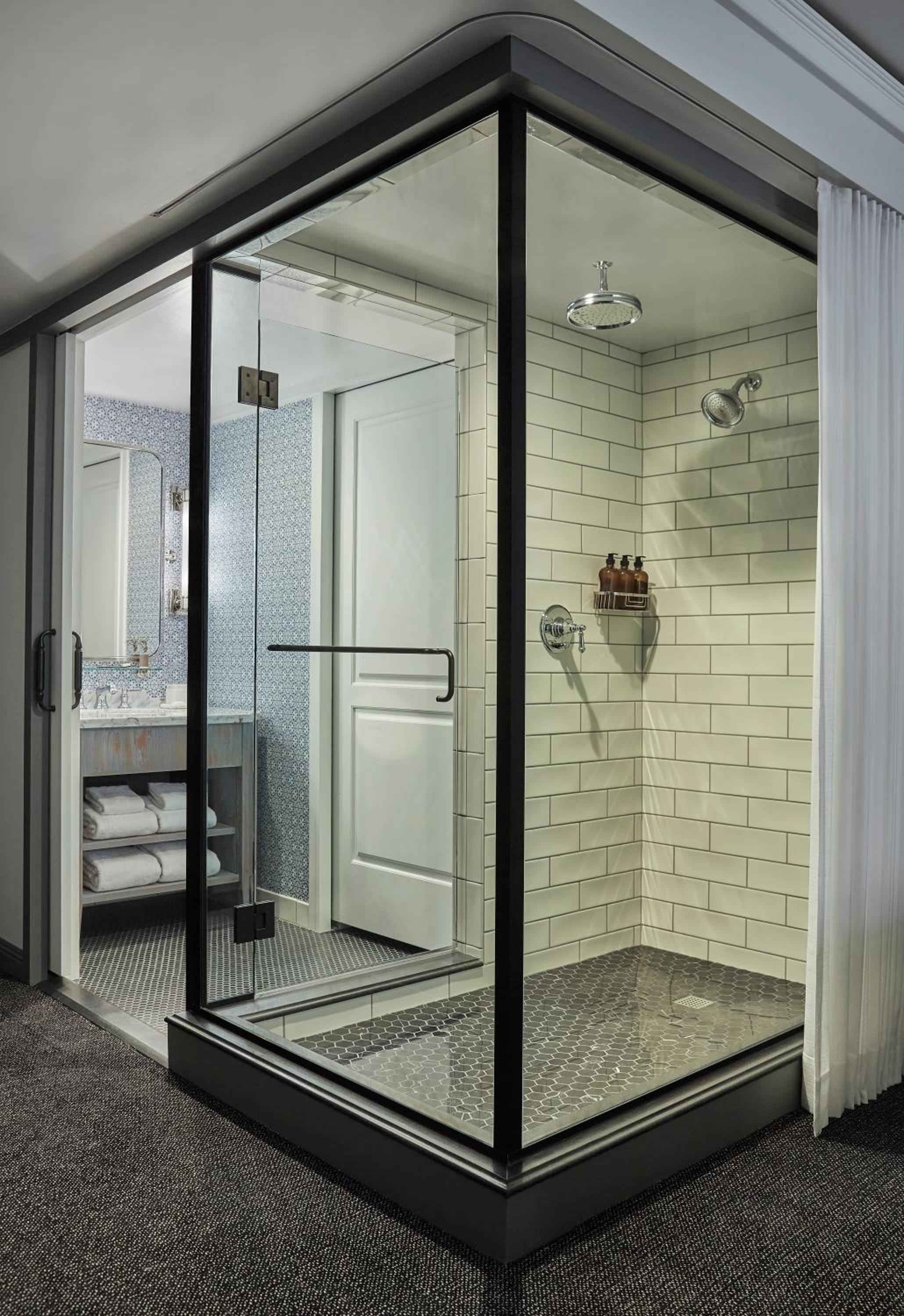 Glass-enclosed rainfall showers with subway tile and industrial-chic black frames create a sleek spa-like sanctuary beneath slanted rooflines.