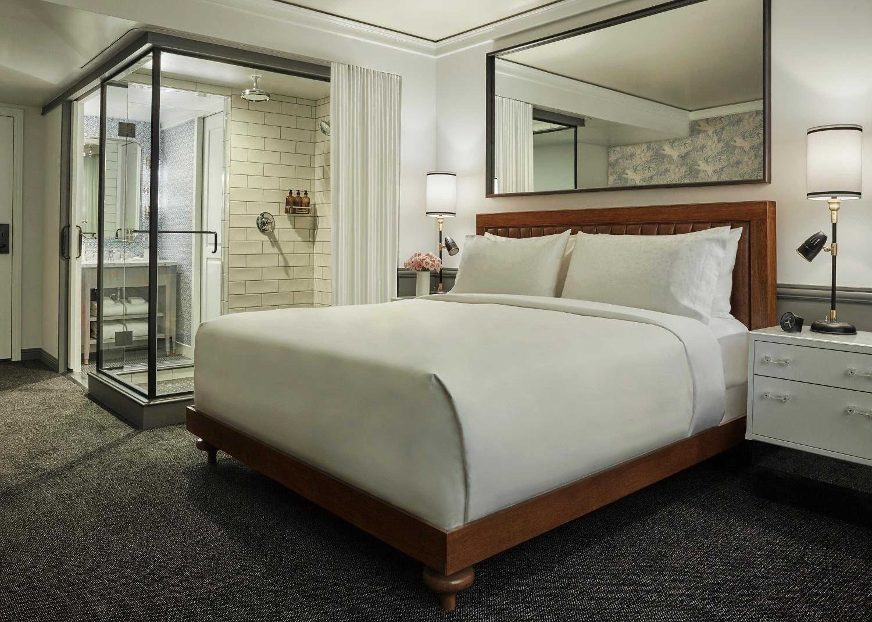 Glass-walled bathrooms and warm walnut headboards create an intimate yet open feel in these thoughtfully designed suites, where industrial touches meet hotel luxury.