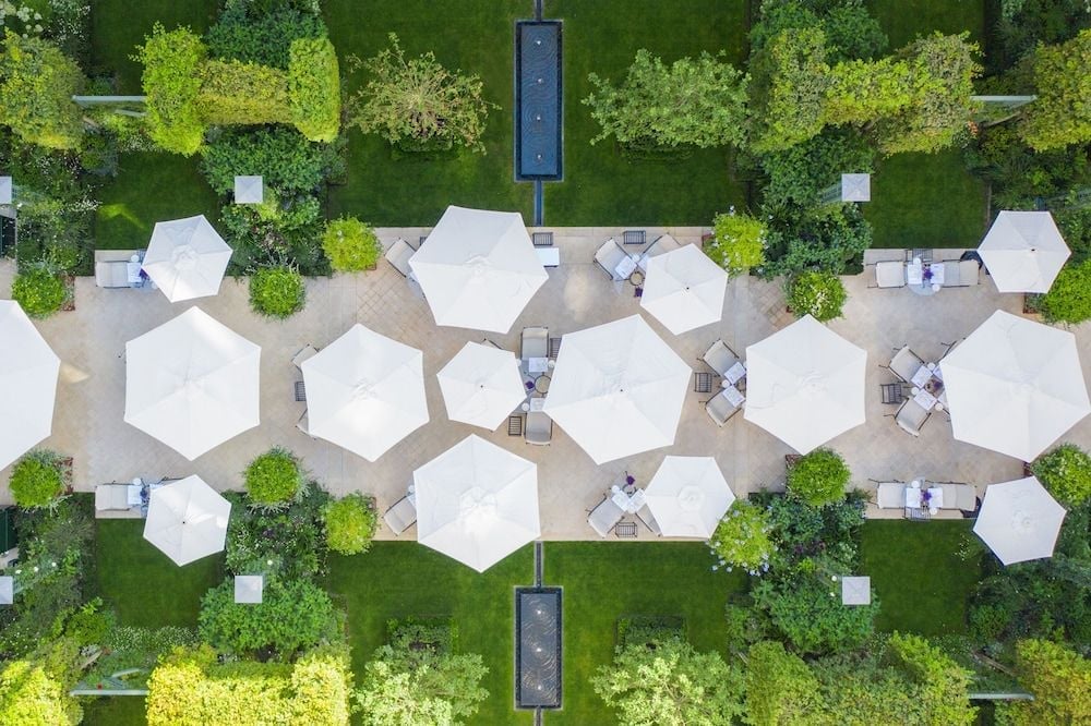 White umbrellas bloom like elegant flowers across manicured grounds, while twin reflecting pools create serene symmetry in this bird's-eye view of refined outdoor luxury.