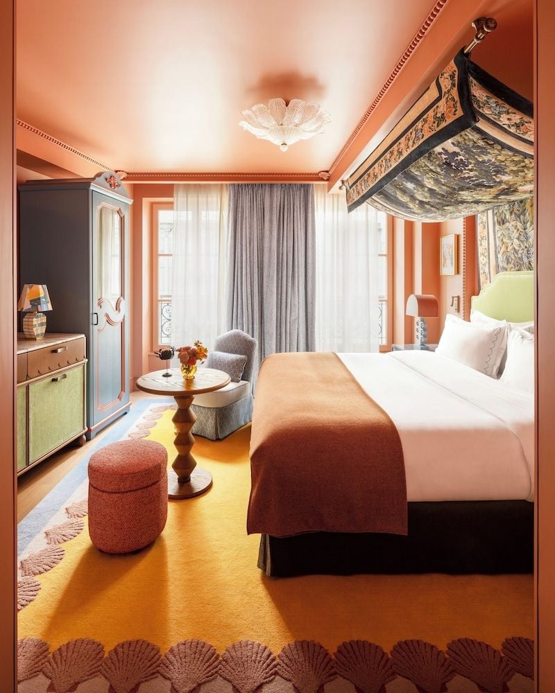 Coral-pink walls and hand-painted ceiling murals create an intimate cocoon, where vintage furnishings and brass fixtures evoke Parisian sophistication in this jewel-box guest room.