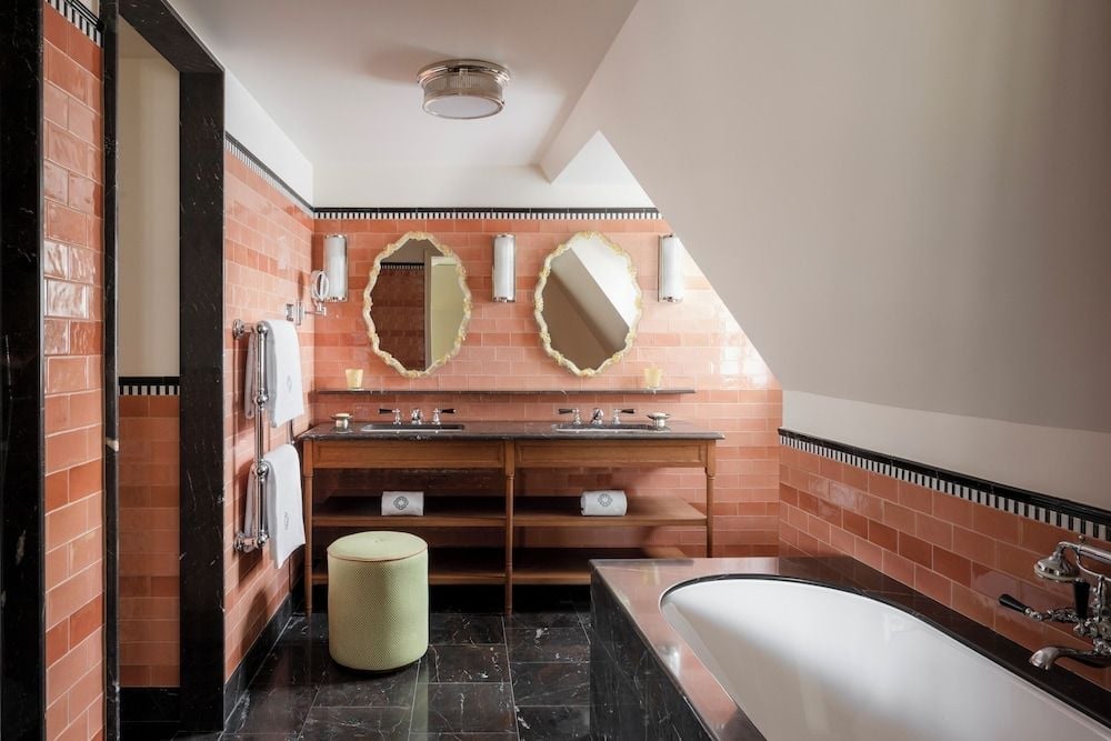 Coral-hued subway tiles and scalloped mirrors create an enchanting powder room where vintage glamour meets Parisian sophistication beneath slanted eaves.