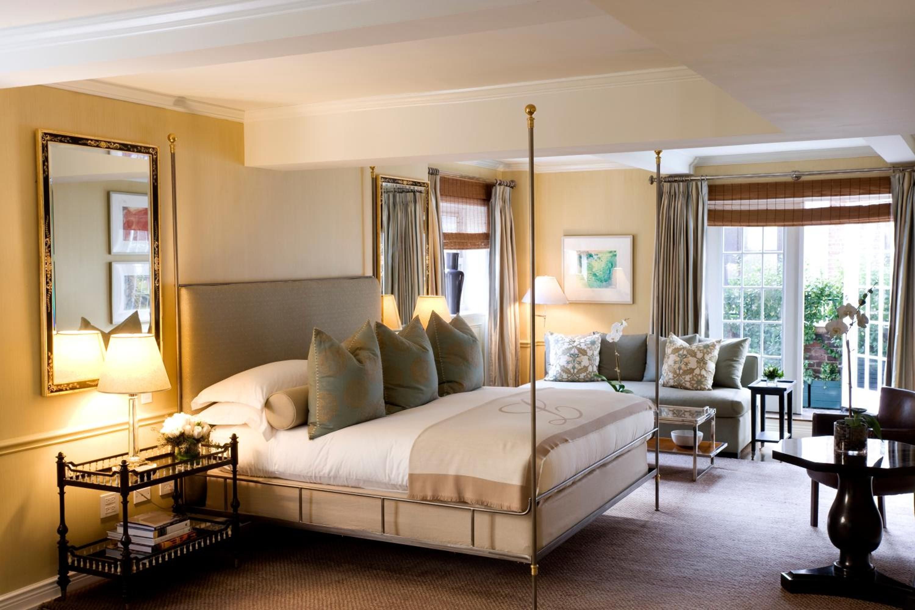 Sage velvet pillows and brass four-poster frames create intimate elegance, while French doors flood this sophisticated suite with golden afternoon light and garden views.