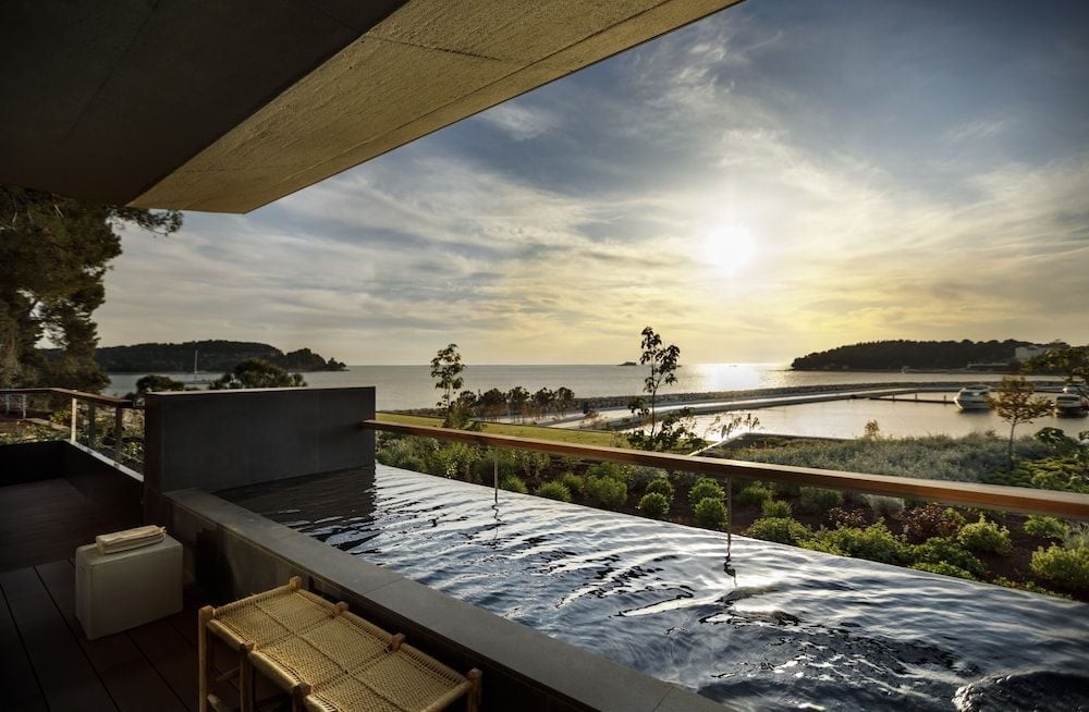 Steam rises from the private terrace hot tub as golden hour light dances across the Adriatic, framing Rovinj's forested coastline in pure luxury.