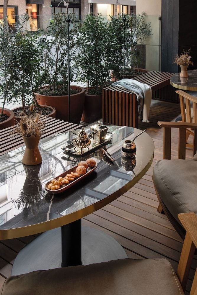 Morning light filters through olive trees onto the rooftop terrace, where brass-rimmed tables hold traditional pastries and golden-hour coffee moments await.