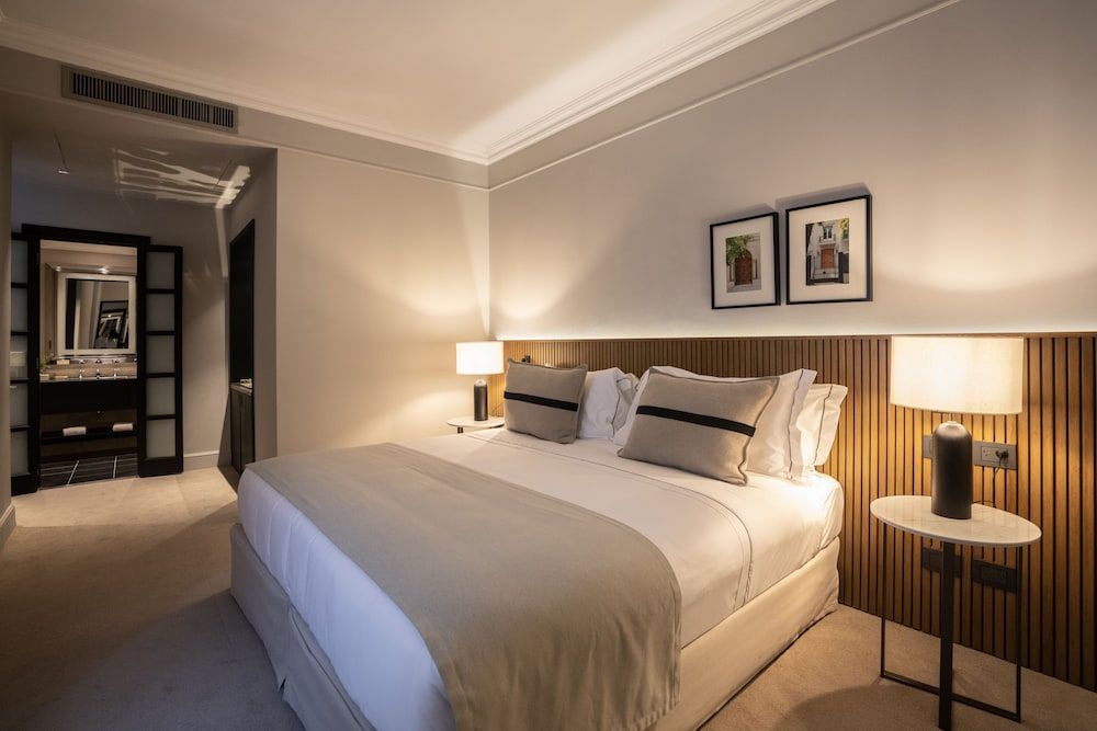 Warm wood paneling and crisp white linens create an intimate sanctuary, where soft bedside lighting casts golden shadows across thoughtfully curated artwork and contemporary furnishings.