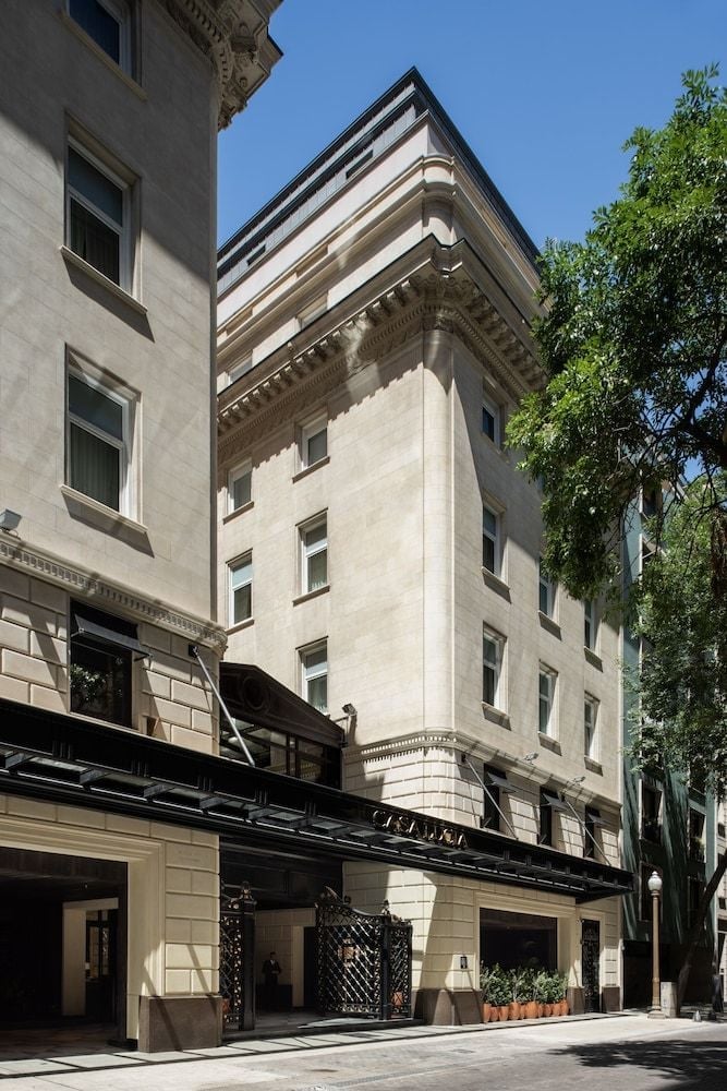 Classical limestone facades and ornate cornices create an elegant streetscape, while the sleek black entrance canopy signals modern luxury within this historic building.