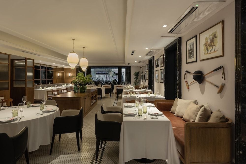 Banquette seating lined with vintage artwork creates intimate dining nooks, while pendant lights cast a warm glow over crisp white linens and gleaming glassware.