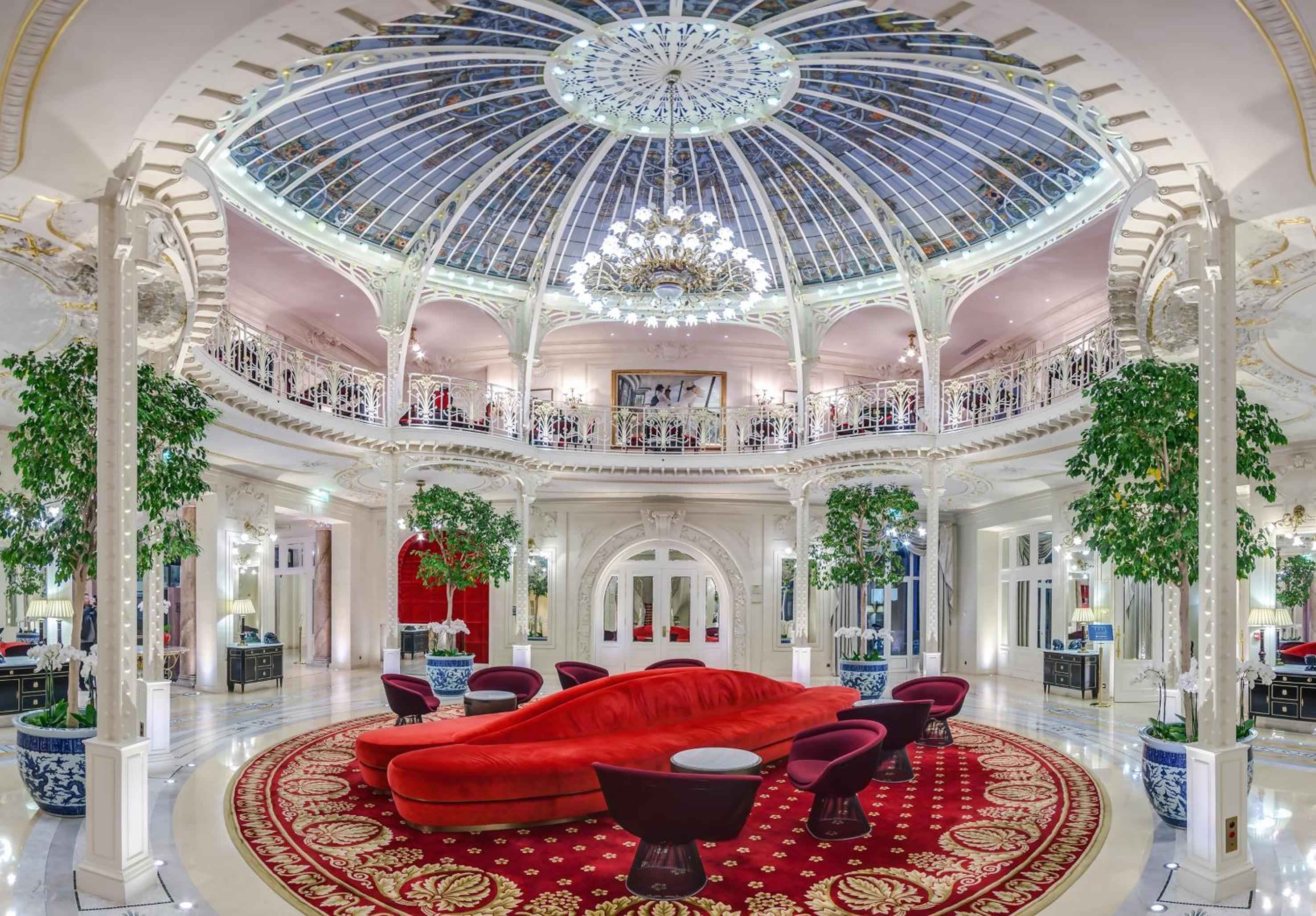 Belle Époque grandeur unfolds beneath a soaring glass dome, where crimson velvet seating and ornate ironwork create an enchanting circular sanctuary of old-world Monte Carlo elegance.